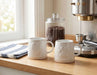 White paw print stoneware mugs displayed on a kitchen countertop